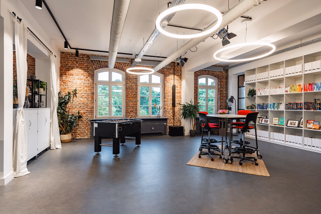 Offene Fläche mit Tischkicker, Stehtisch und runden Leuchten im Loft von StartMiUp Minden