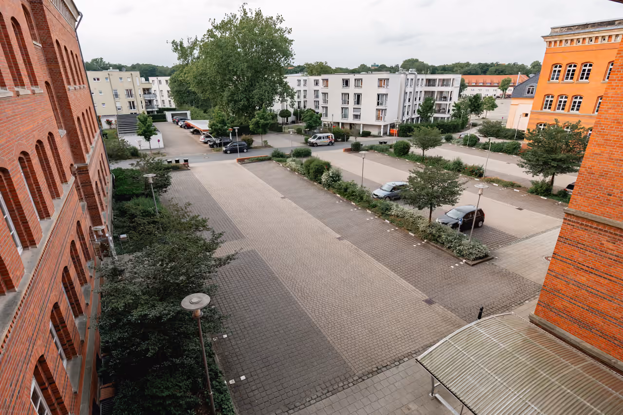 Blick aus einem Fenster von StartMiUp Minden auf Straße, Parkplatz und die Backsteinbauten nebenan